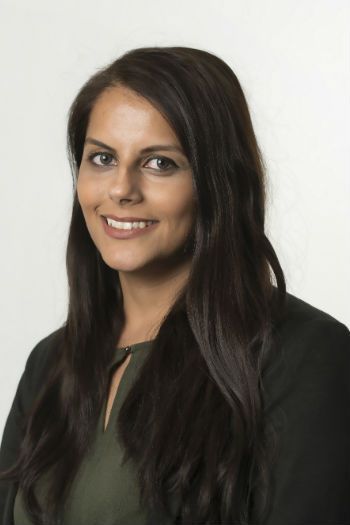 A woman with long brown hair is wearing a black sweater and smiling for the camera.