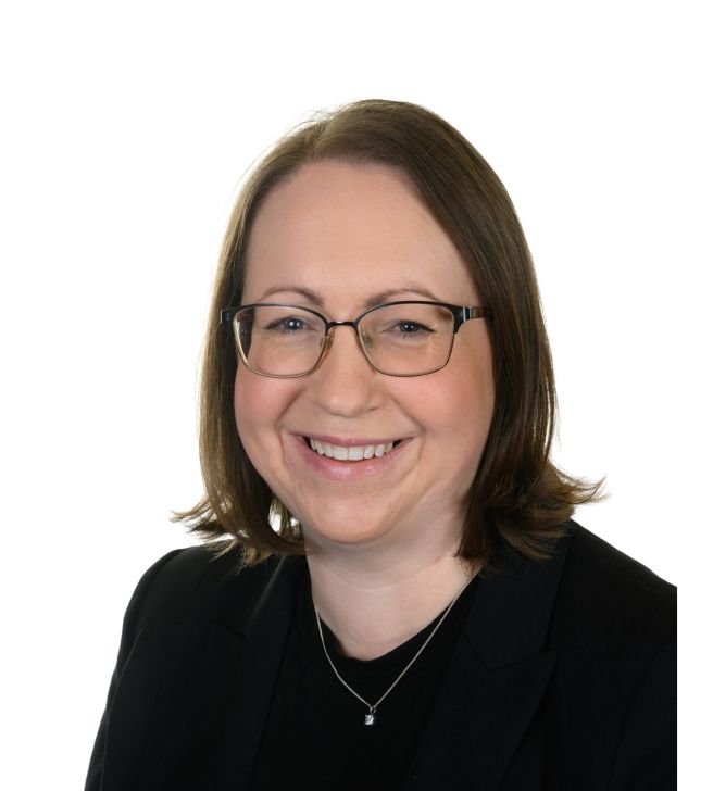 A woman wearing glasses and a black jacket is smiling for the camera.