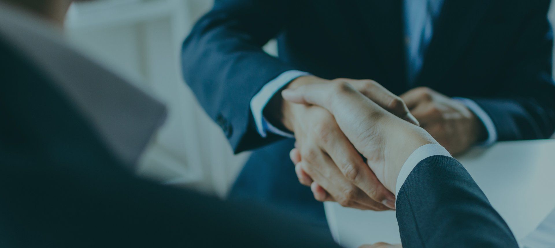 Two businessmen are shaking hands while sitting at a table.
