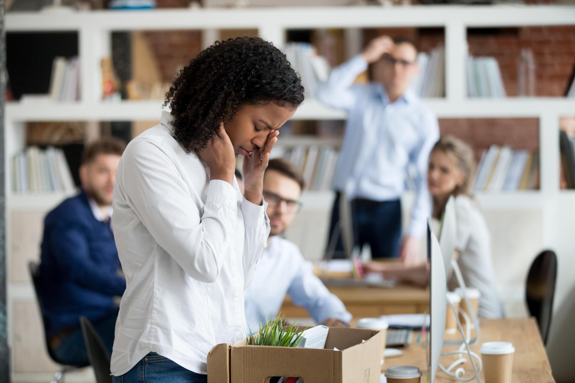 A woman is standing in an office with a box of her belongings.