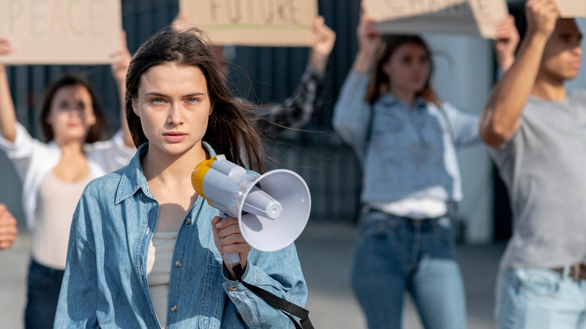 A woman is holding a megaphone in front of a group of people holding signs.