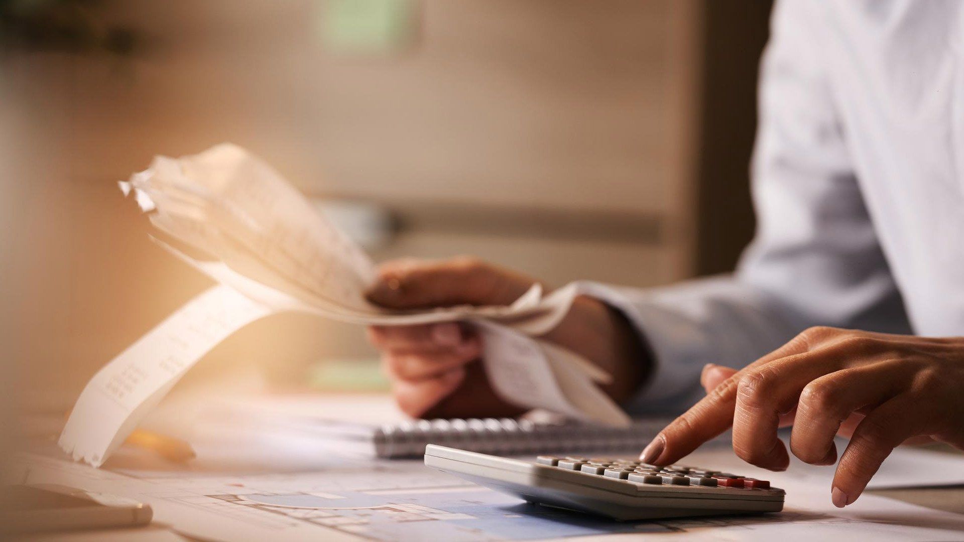 A person is using a calculator while holding a piece of paper.
