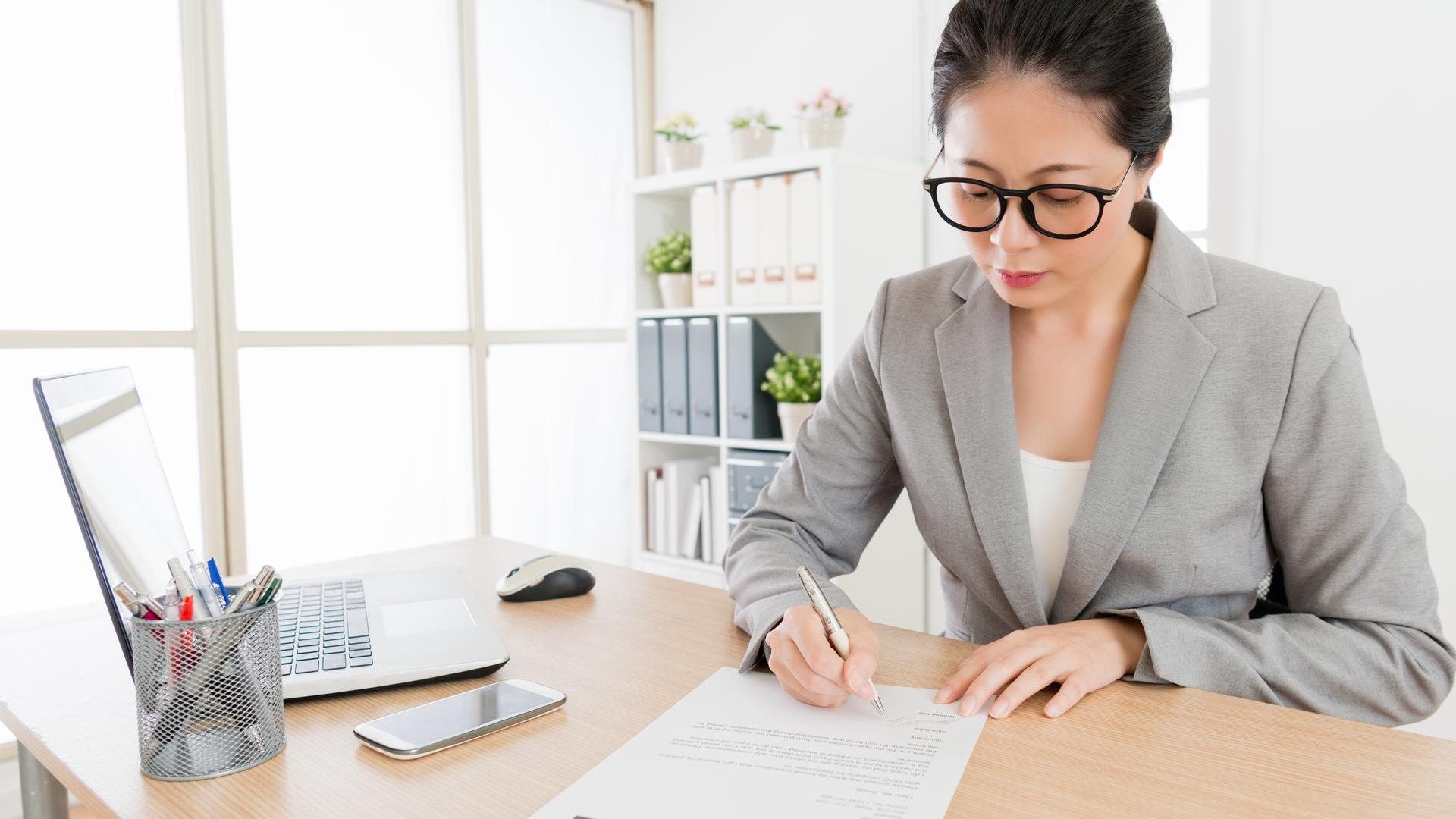 A woman is sitting at a desk writing on a piece of paper.