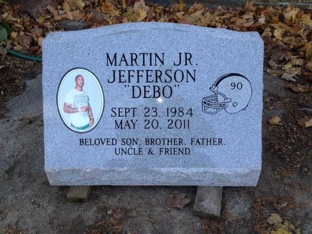 Gray headstone with photo, football helmet, and inscription: 