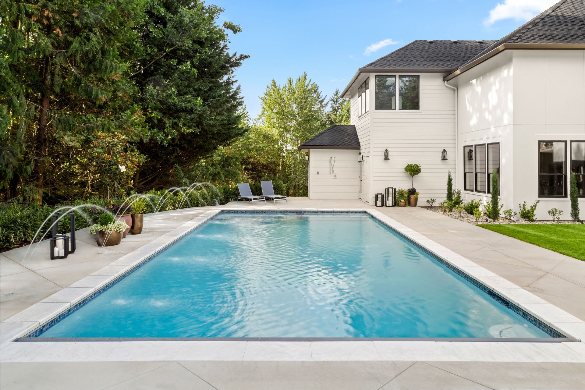 A clean rectangular swimming pool sits in a landscaped backyard beside a modern two story home.