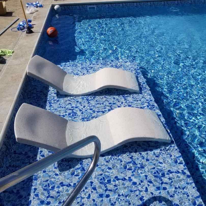 Two lounge chairs are sitting on the edge of a swimming pool.