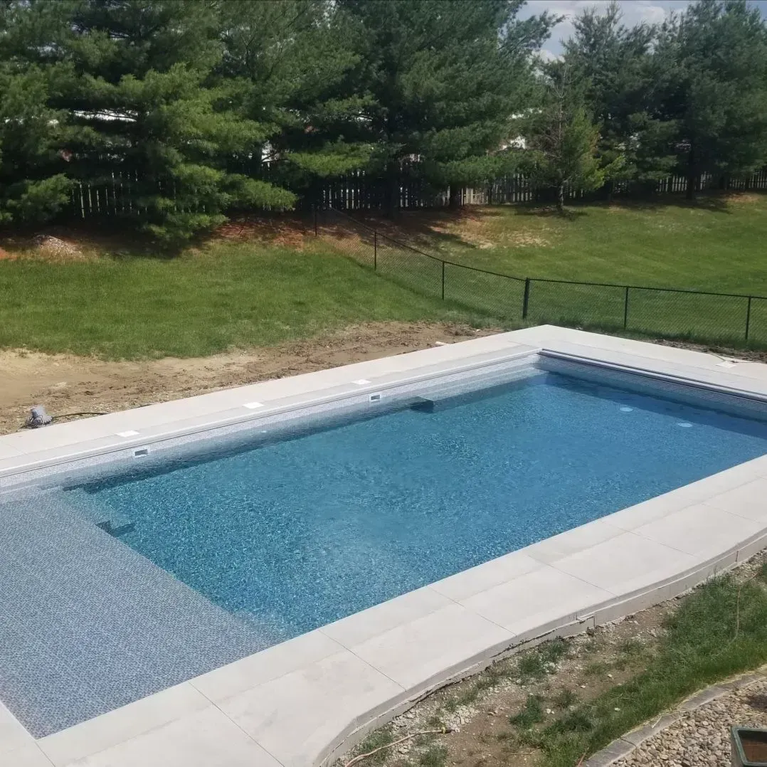 A large swimming pool is surrounded by trees and grass.