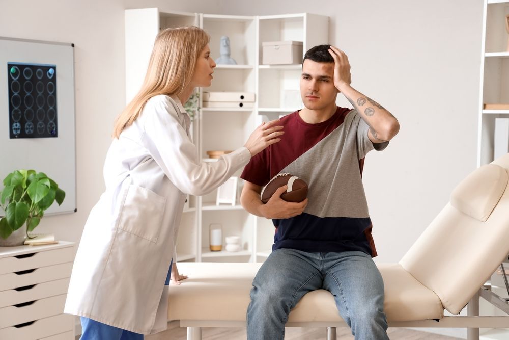 Doctor examining seated patient in clinic, with patient holding his head in discomfort