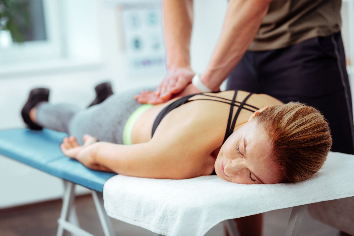 Massage therapist pressing a woman’s lower back on a treatment table in a clinic