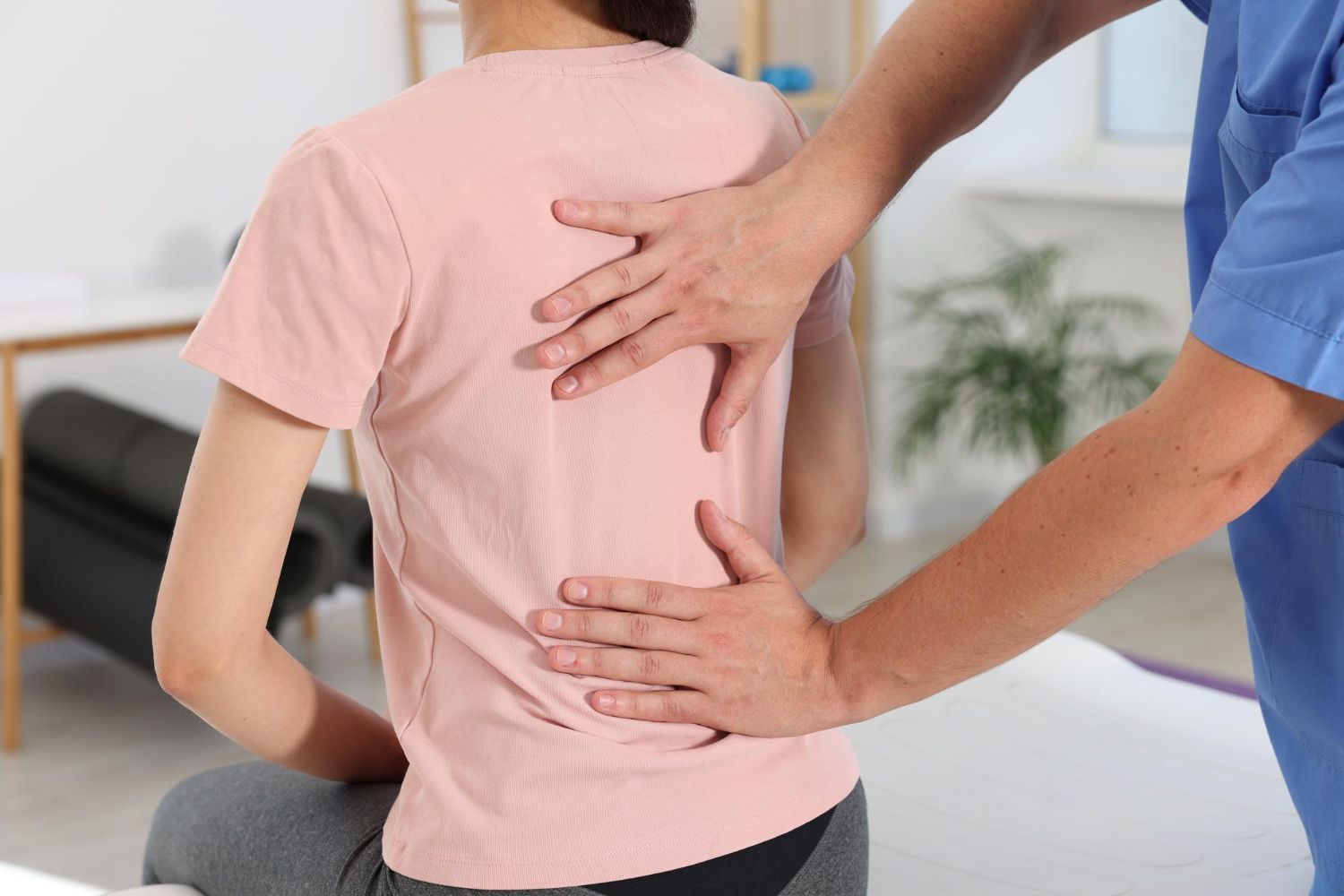 Therapist examining a patient’s lower back in a clinic, with hands on the spine and waist.