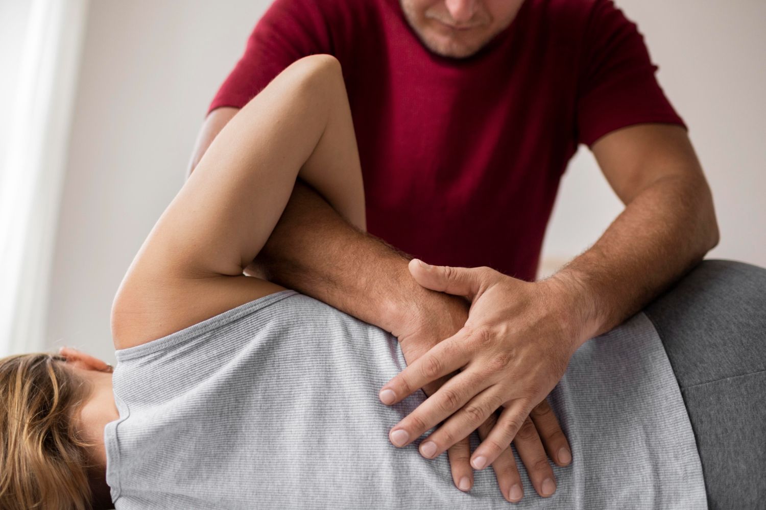 A man in a red shirt performs a back adjustment on a woman lying on her side.