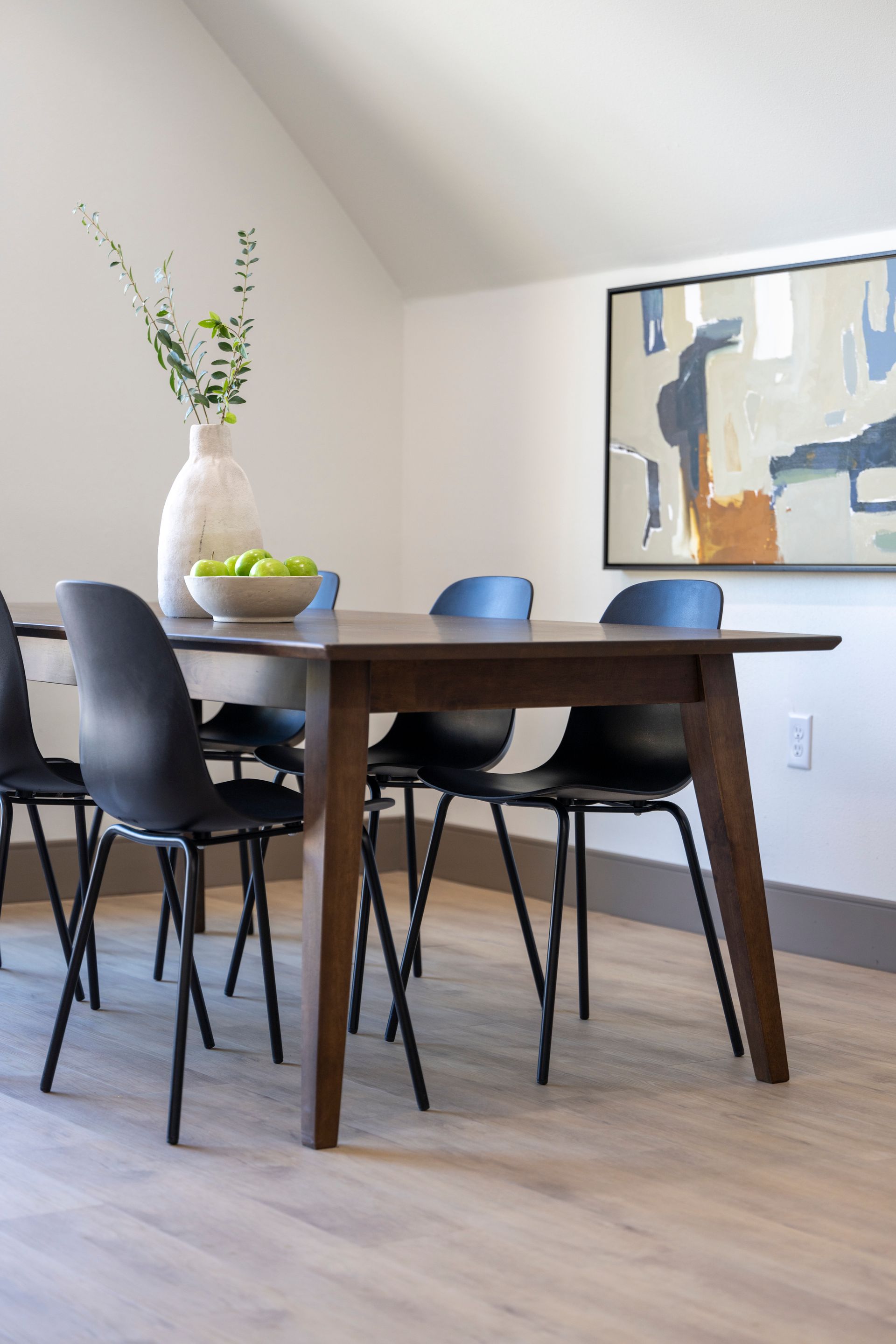 Dining room with dark wood table, black chairs, white vase, and abstract wall art.
