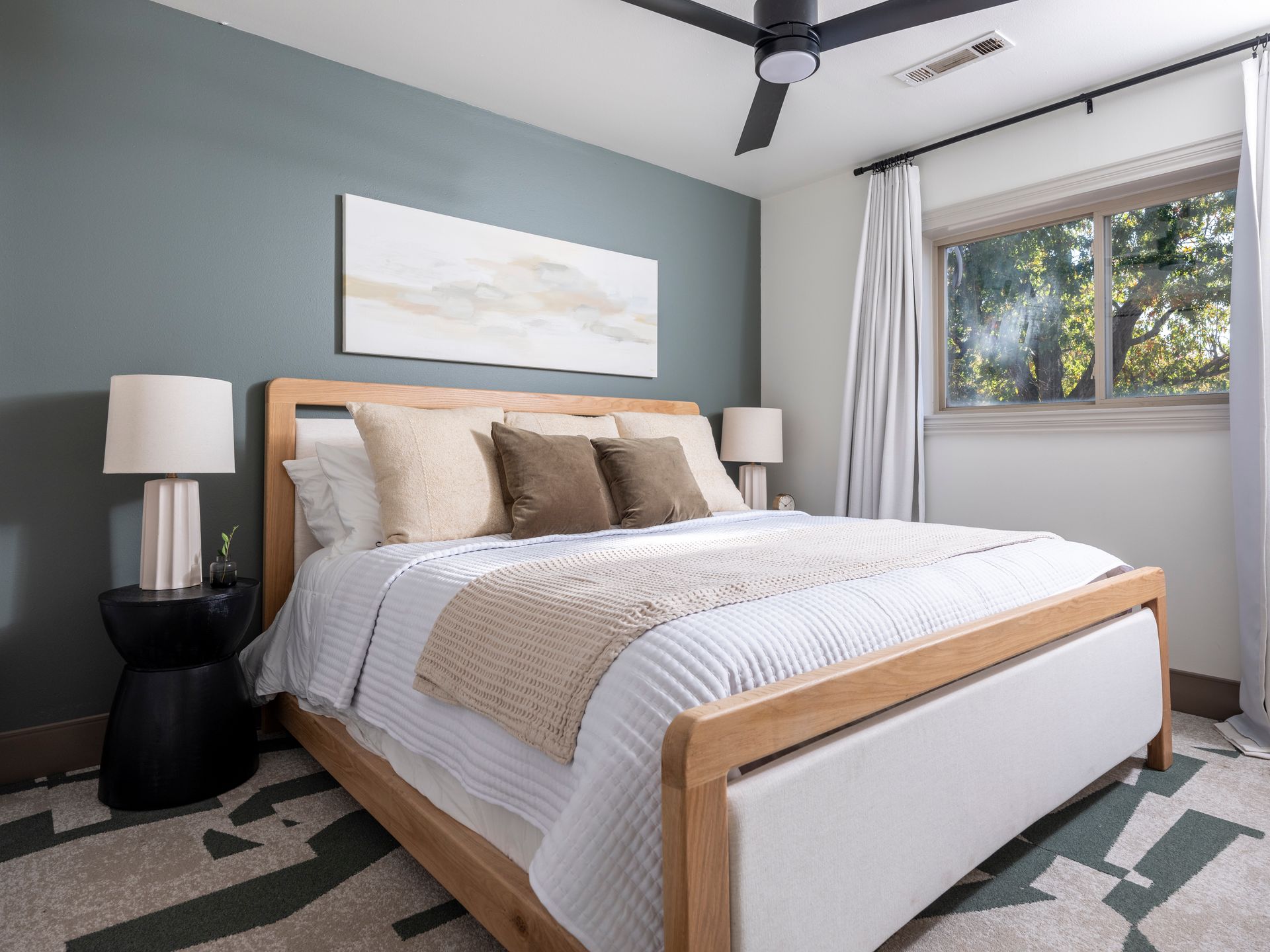 Modern bedroom with a wooden bed, beige bedding, nightstands, lamps, and a large window