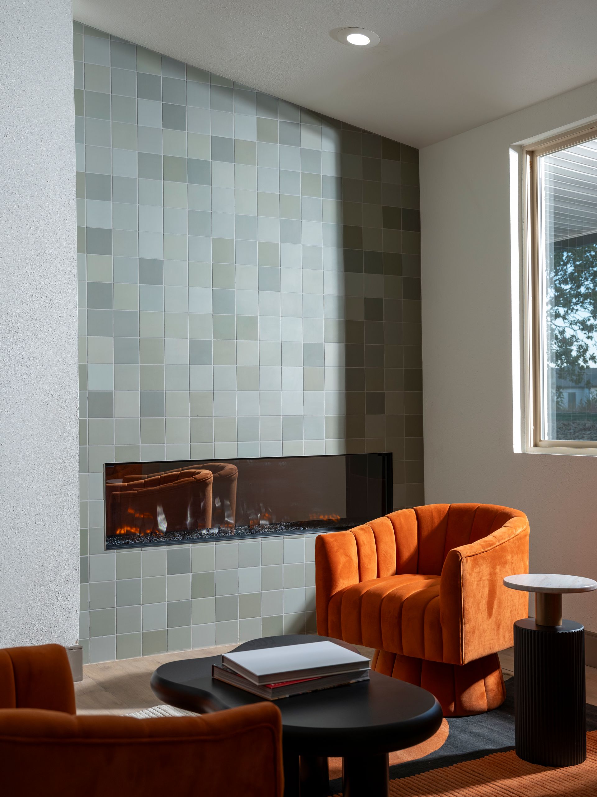 Modern living room with tiled fireplace, orange armchair, black coffee table, and window view