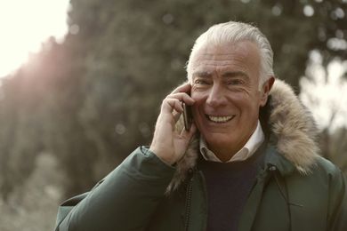 Older man smiling while talking on the phone outdoors