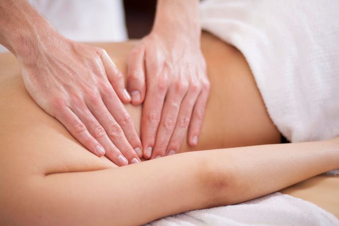Manos dando un masaje en la espalda de una persona en una camilla de spa.