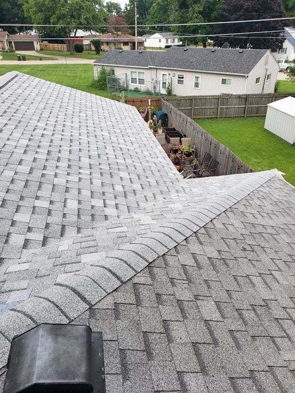 Gray asphalt shingle roof on a house, with a view of a backyard, grass, and neighboring houses.