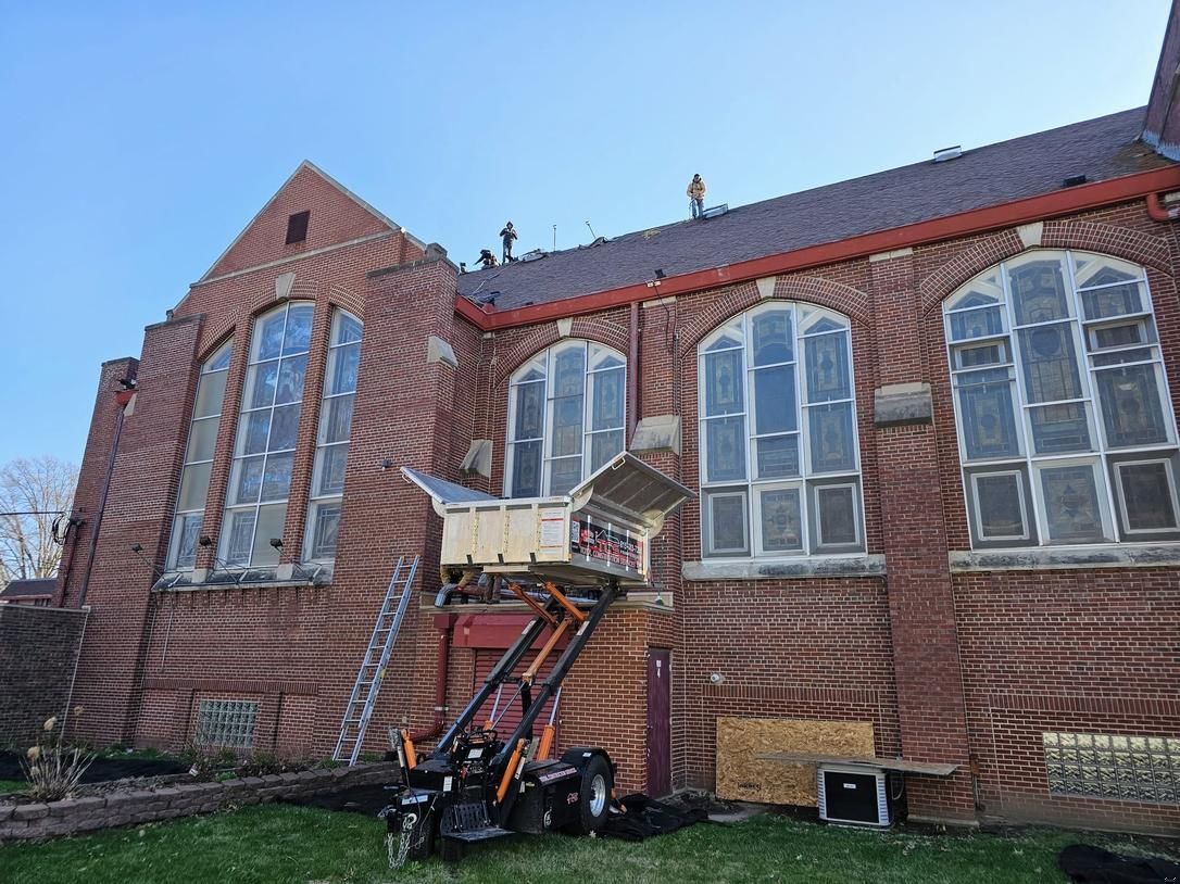 Brick church building with tall arched windows, construction equipment, and a ladder.