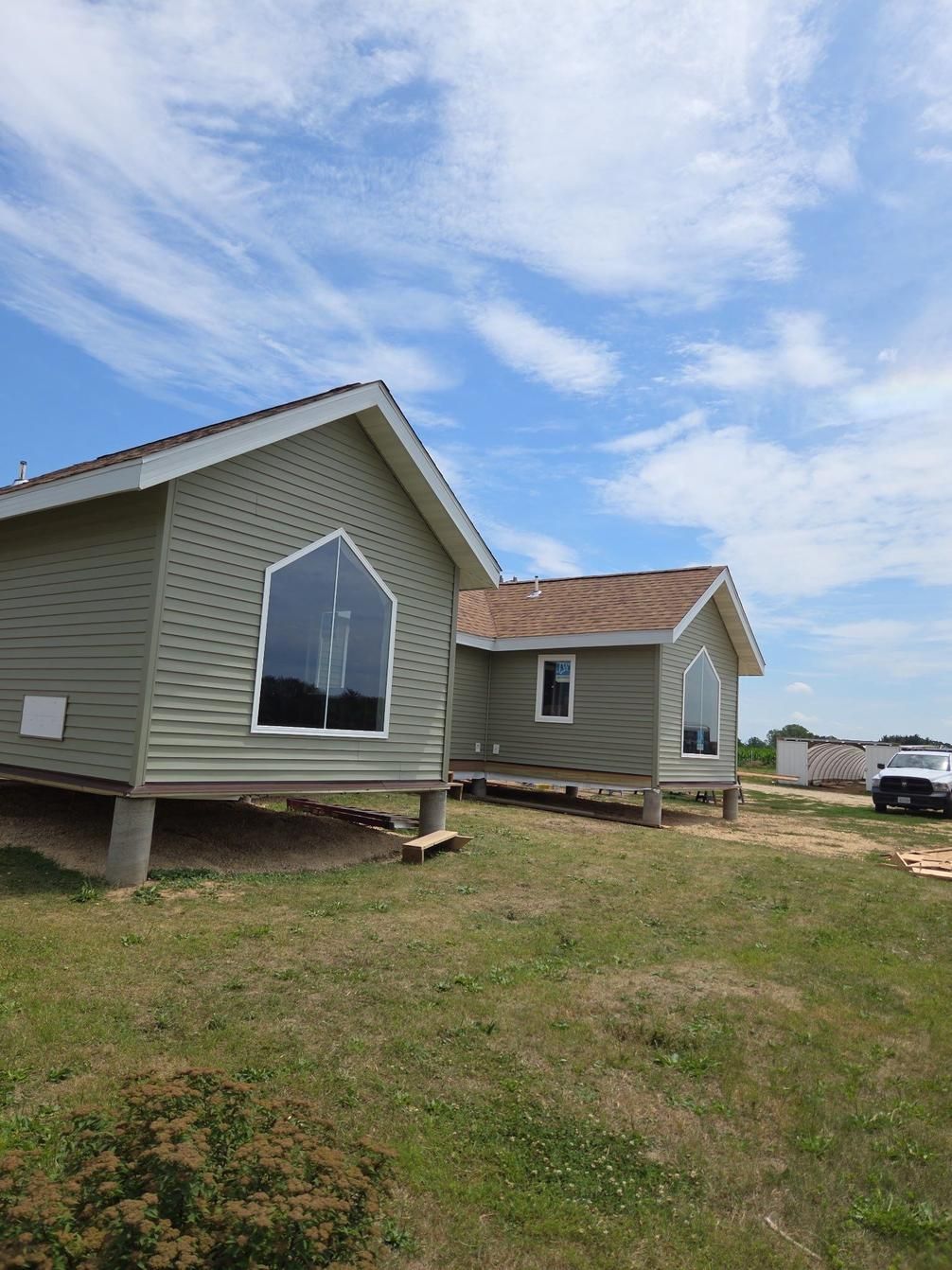 Two small, green-sided houses with angled roofs and large geometric windows on wooden supports against a blue sky.