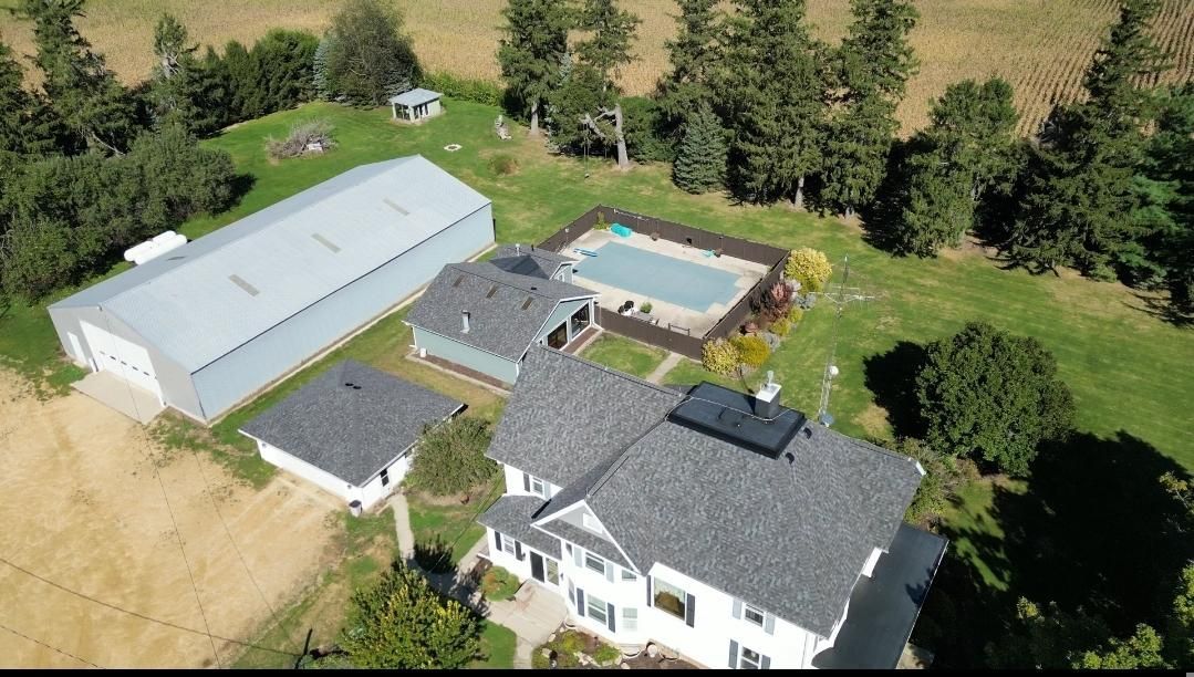 Aerial view of a white house with a pool, a large metal building, and farmland in the background.