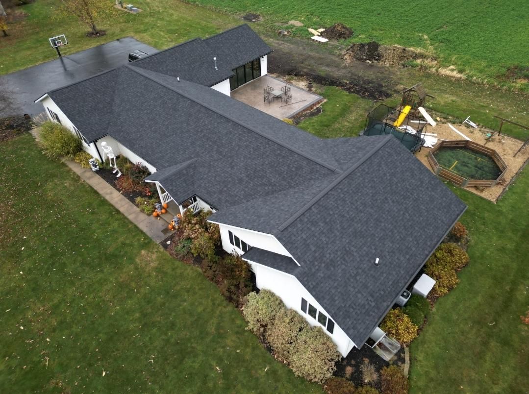 Overhead view of a white house with a dark gray roof surrounded by green grass and a small pool.