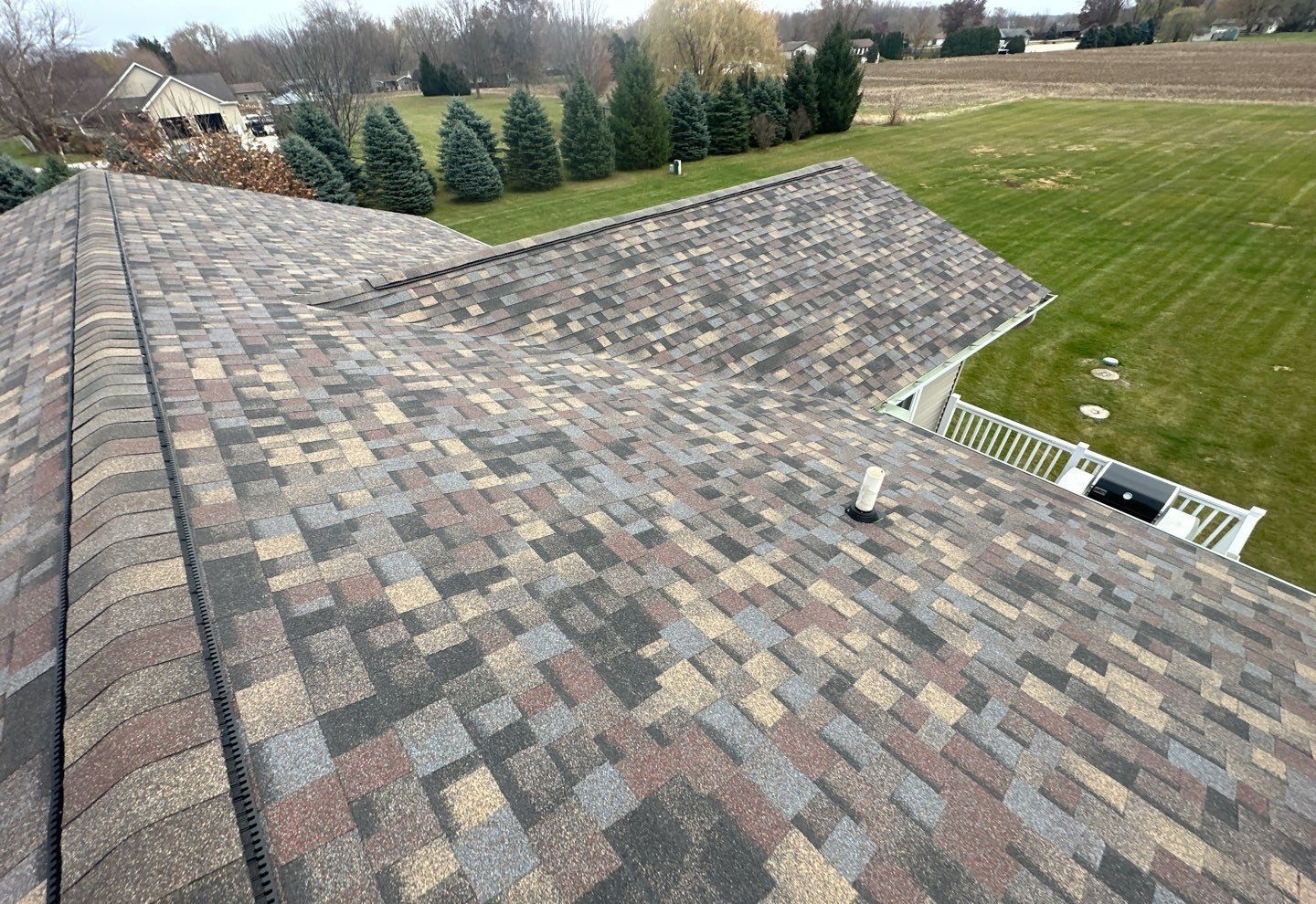 View of a shingled roof with various earth-tone colors and a white trim, overlooking a grassy yard.
