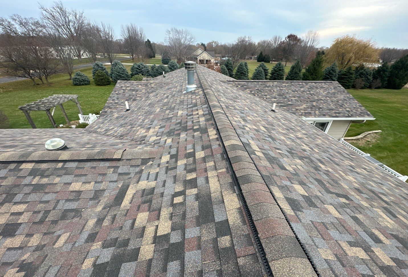 Overhead view of a roof with brown and tan shingles, chimney, and surrounding trees.
