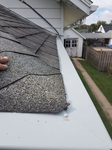 Roof shingles, white gutter, hand touching the edge, exterior of a house.