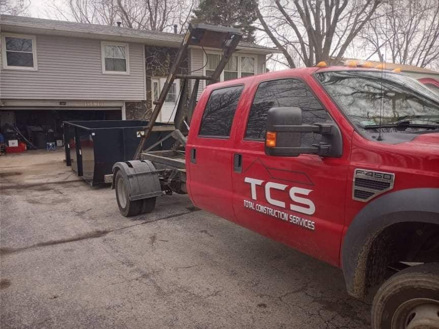 Red TCS truck with a dumpster in a residential driveway.