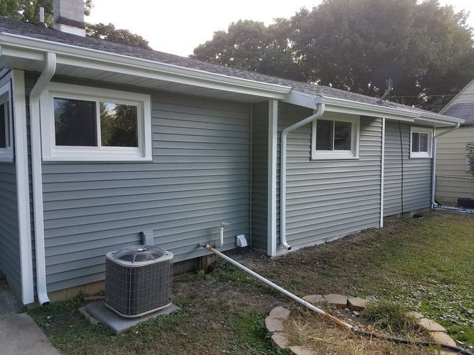 Side view of a house with light blue siding, white trim, and a cooling unit.