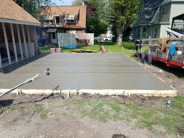 Newly poured concrete slab in a backyard, surrounded by wooden forms, near a garage and houses.