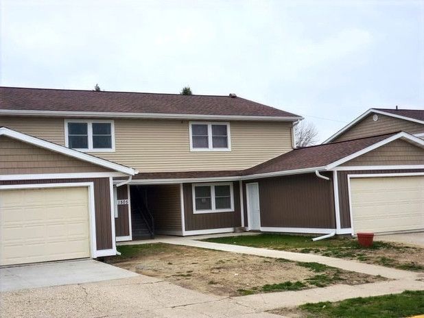 Townhouse complex with beige siding, brown trim and garage doors. Cloudy sky overhead.