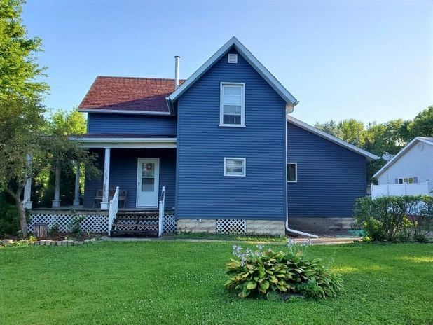 Blue house with a red roof, front porch, and green lawn on a sunny day.
