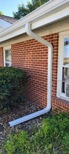 White gutter on red brick wall of a house. Green bushes are at the bottom.
