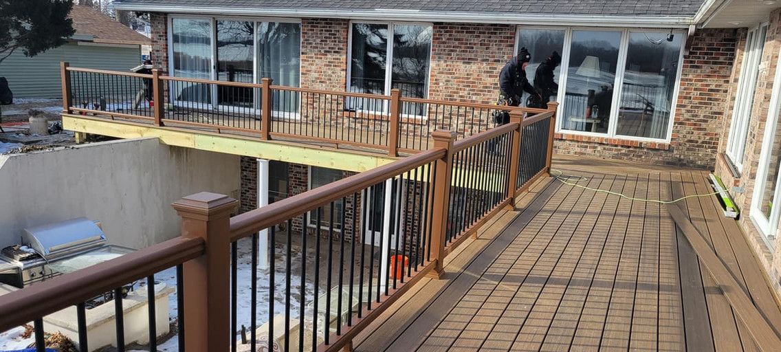 Wooden deck with black railings and a house in the background. Snow and yard are visible.