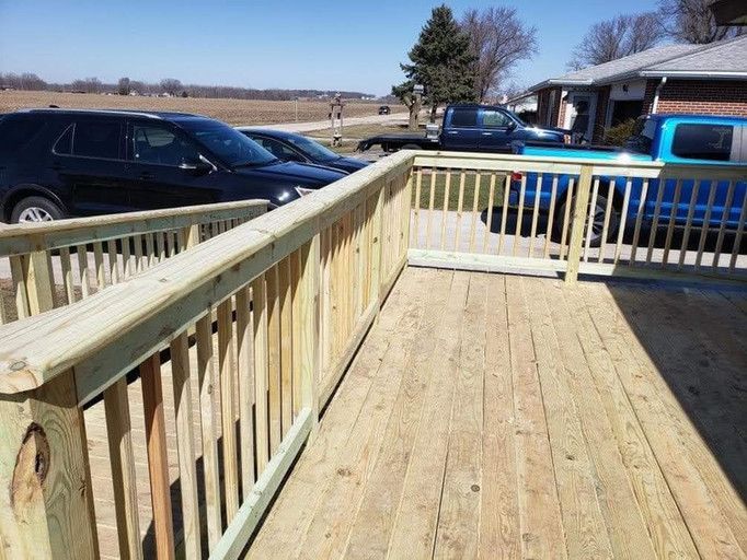 Wooden deck with railing, parked vehicles in background.
