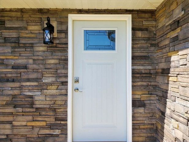White front door with rectangular window, on a stone-veneer wall, with a black lantern to the left.