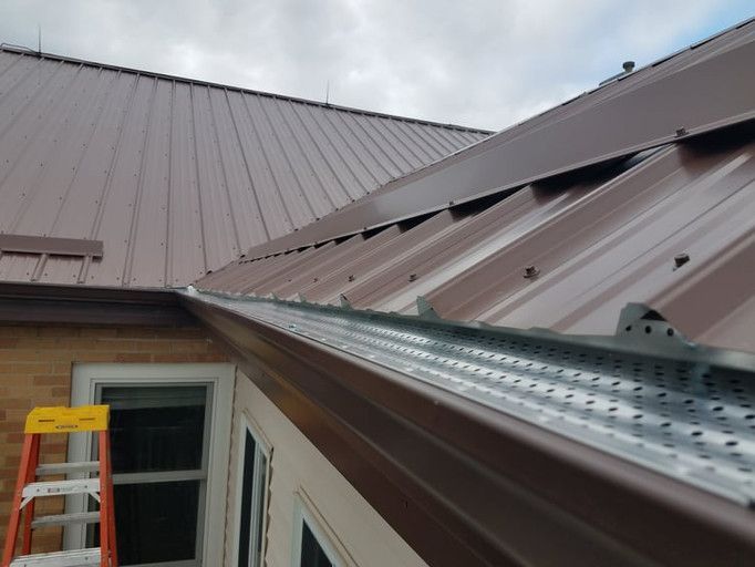 Brown metal roof with gutter guard installed; ladder visible near window.