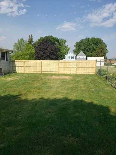 Wooden fence in a backyard, with green grass and trees in the background under a blue sky.