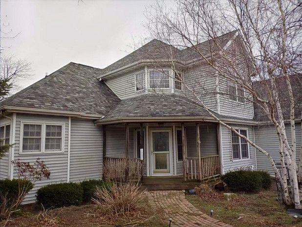 Two-story gray house with a front porch and leafless trees in front