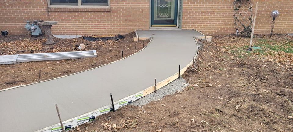 Freshly poured concrete walkway leading to a brick home's front door.