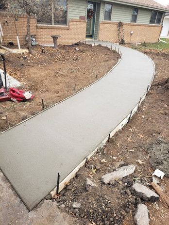 Newly poured concrete walkway curves towards a house with tan brick and green siding.