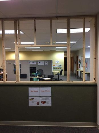 Wooden frame for a window, looking into an office. Posters on the wall below.