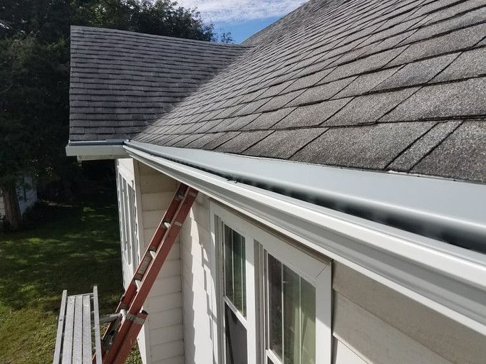 White house with gray roof and gutter, ladder leaning against it.