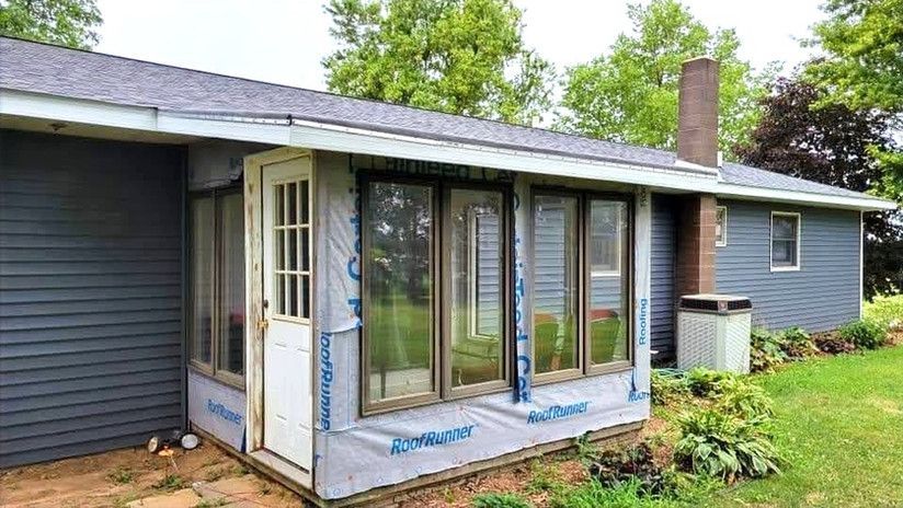 Sunroom addition with several windows, attached to a gray-sided house.