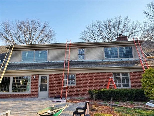 House exterior with three ladders leaned against the roof, undergoing construction with new siding and windows.