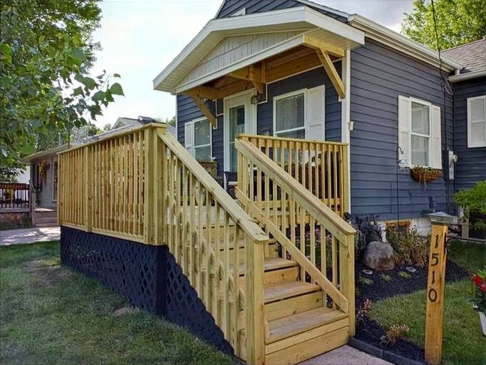 Wooden porch and stairs of a dark blue house, with a grassy lawn and a house number sign.