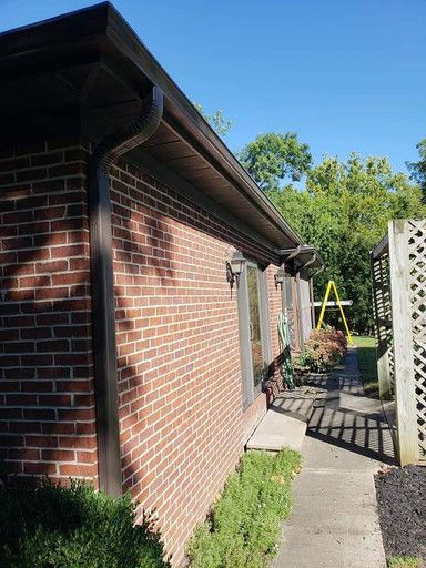 Brick building with brown trim, gutters, and windows; a walkway runs along the wall.