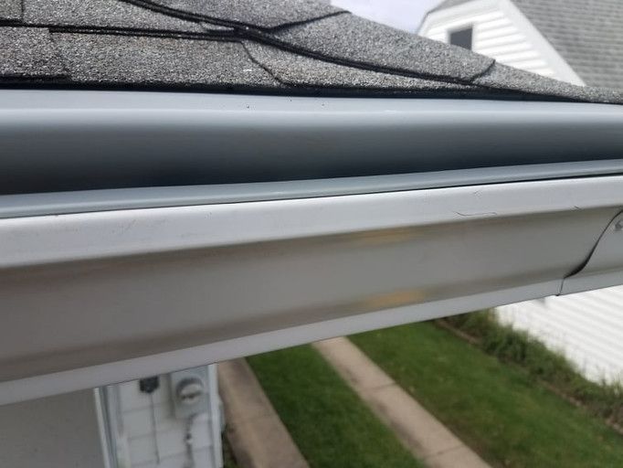 White house gutter with gray shingles and a grassy yard.