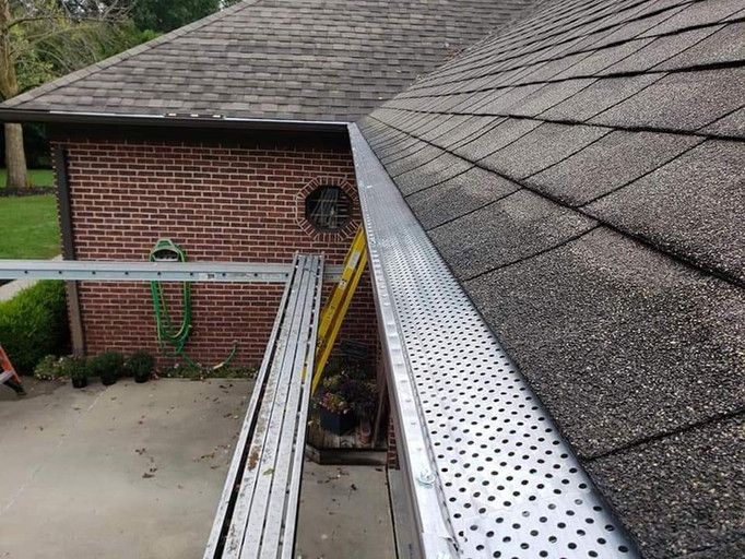 A ladder alongside a roof, gutter with gutter guard, against a brick house.